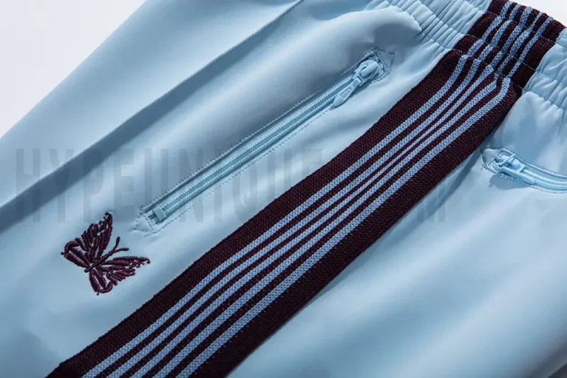 Close-up detail of the track pants pocket and delicate butterfly embroidery.