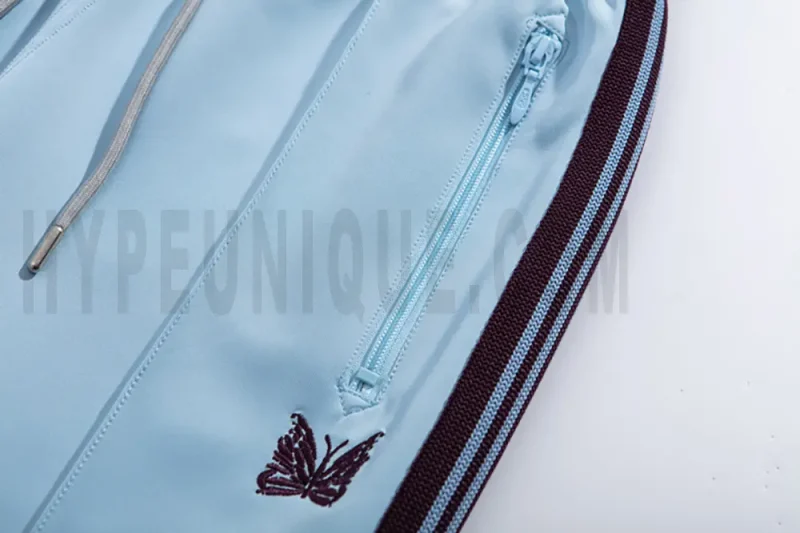 Close-up detail of the track pants pocket and delicate butterfly embroidery.