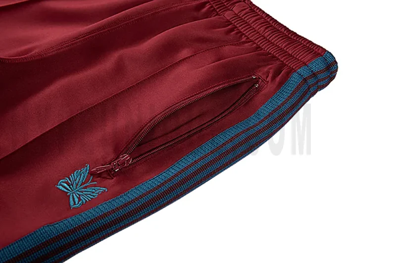 Close-up detail of the track pants pocket and delicate butterfly embroidery.