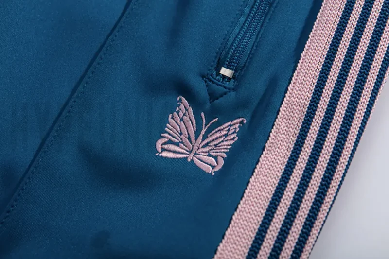 Close-up detail of the track pants pocket and delicate butterfly embroidery.
