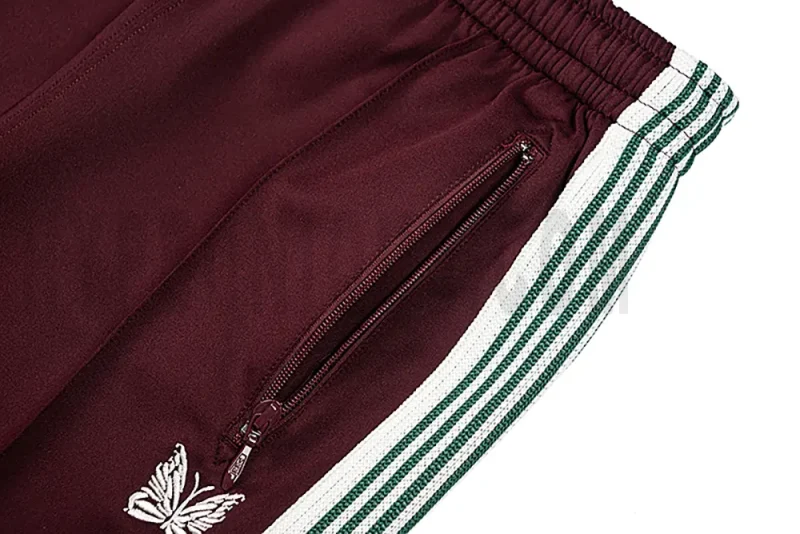 Close-up detail of the track pants pocket and delicate butterfly embroidery.