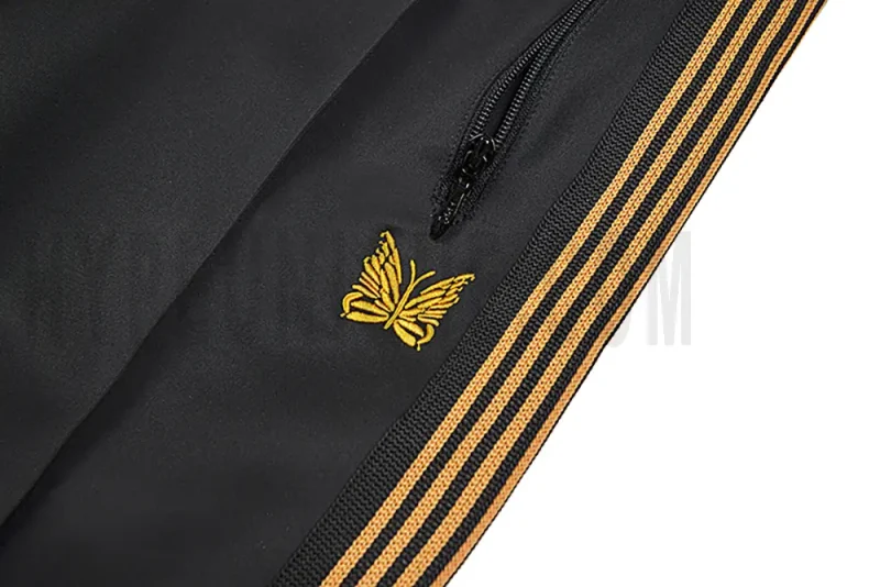 Close-up detail of the track pants pocket and delicate butterfly embroidery.
