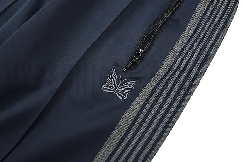 Close-up detail of the track pants pocket and delicate butterfly embroidery.