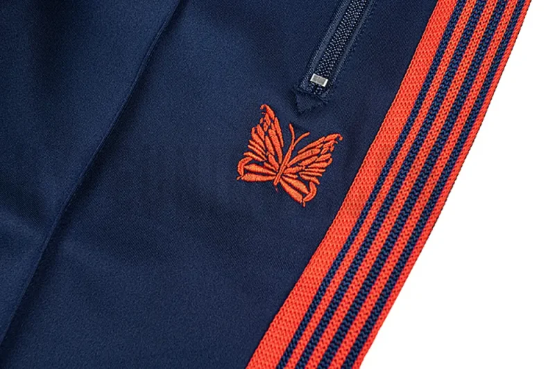 Close-up detail of the track pants pocket and delicate butterfly embroidery.