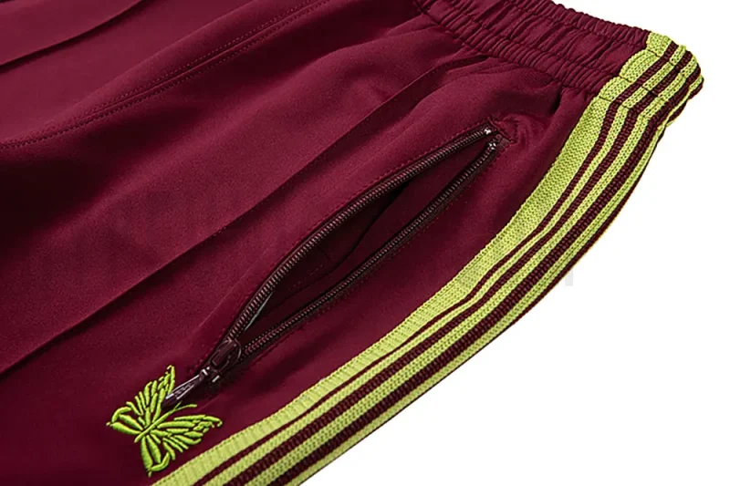 Close-up detail of the track pants pocket and delicate butterfly embroidery.