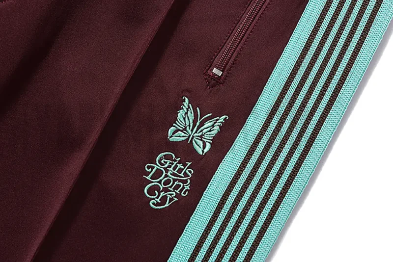 Close-up detail of the track pants pocket and delicate butterfly embroidery.